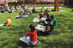 Students sitting outside on a grass sketching