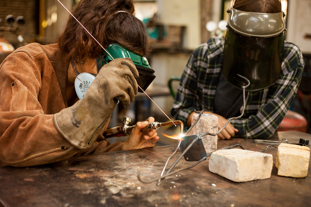 Two students welding art pieces in a classroom 